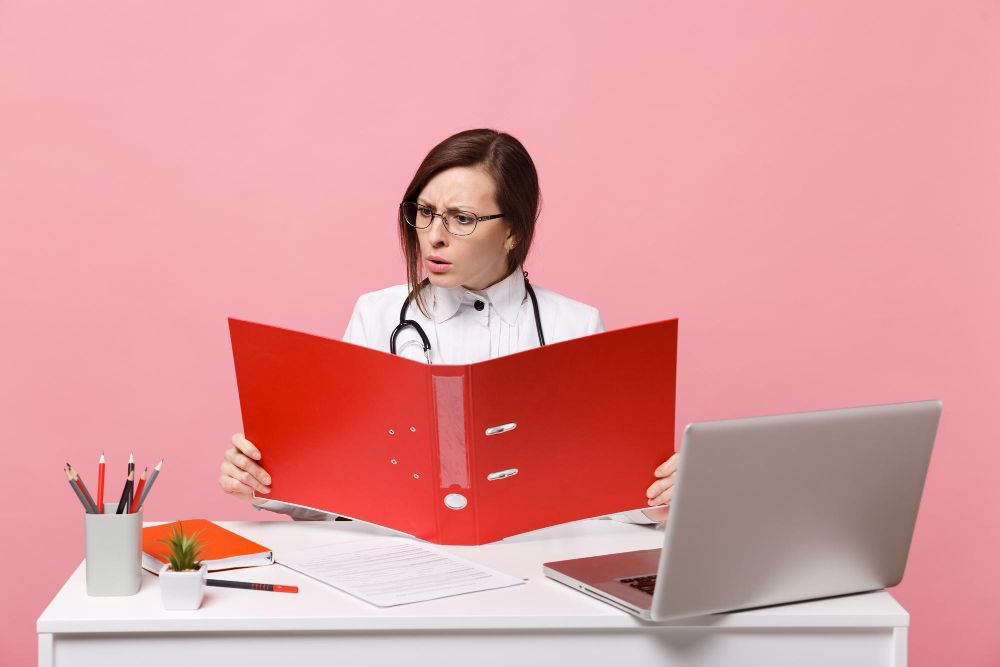 Female Doctor Sit at Desk Work on Computer With Medical Document