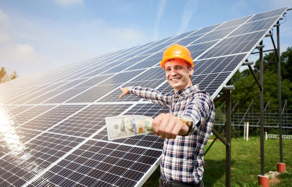 Smiling Guy With Hundred Dollar Bill in Hand Shows at Station of Solar Batteries