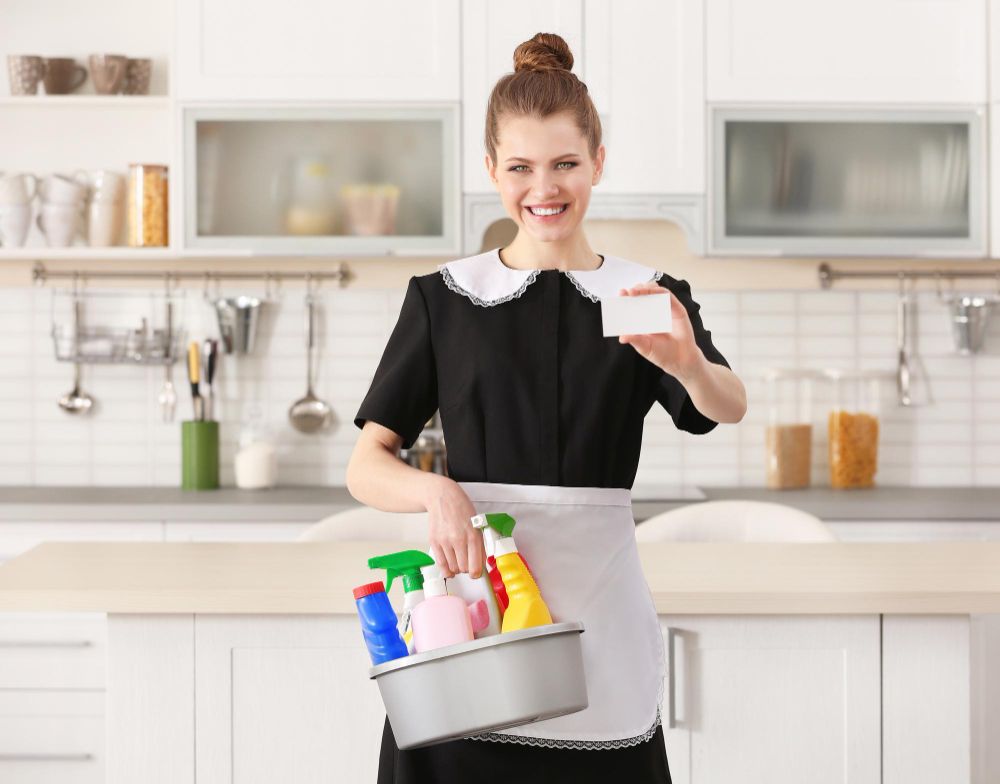 Young Chambermaid With Business Card and Cleaning Supplies in Kitchen