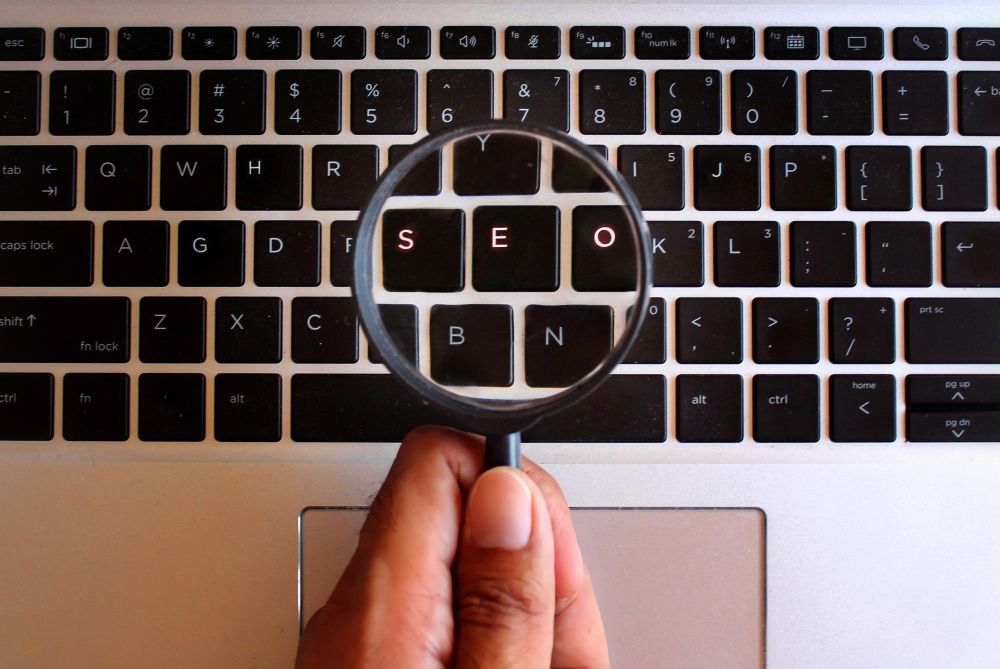 hand holding magnifying glass and glowing keypad with text seo search engine optimization