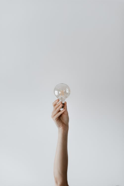 A Woman’s Hand Showing Transparent Light Bulb Against Gra Backdrop