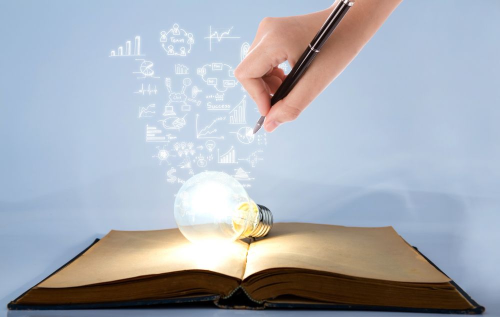 Person Drawing Symbols Coming Out of a Light Bulb on Top of a Book
